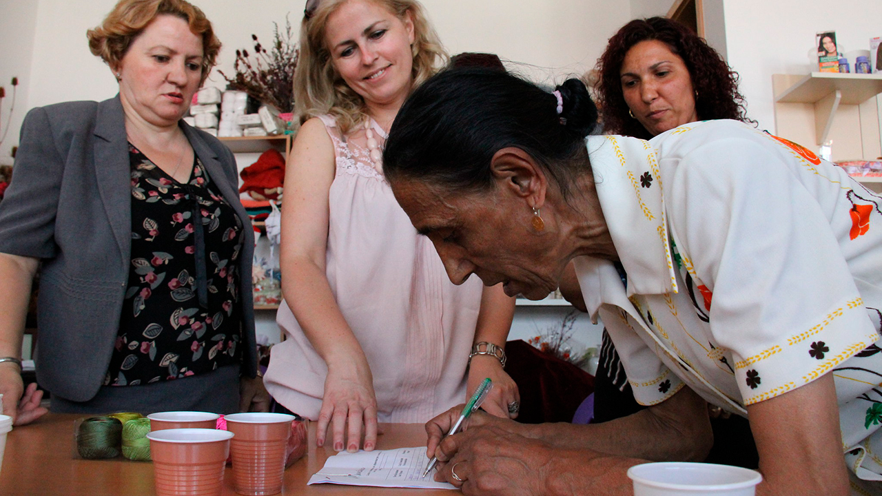 Kosovolainen nainen kirjoittaa paperille kurssin järjestäjien seurassa.